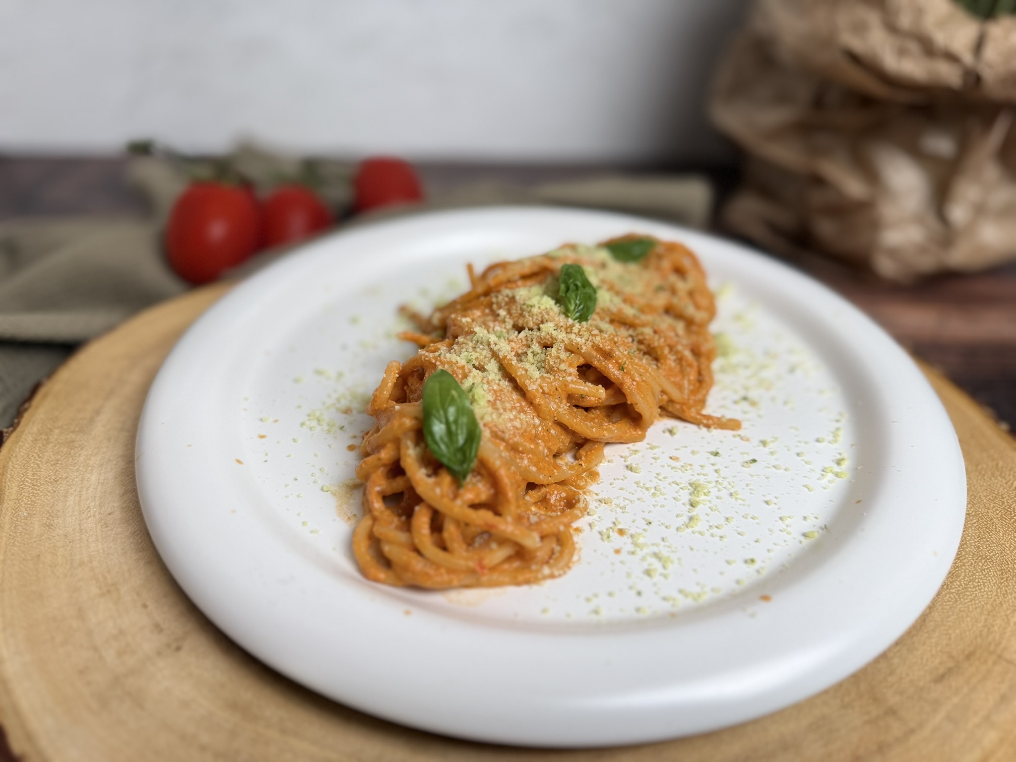 SPAGHETTI CREMOSI CON CONDIMENTO SENZA COTTURA: RICETTA ESTIVA FACILE E VELOCE, serviti in un piatto bianco, conditi con una crema vellutata di pomodorini, robiola, parmigiano, pomodori secchi, pinoli e basilico. Gli spaghetti sono completati con una spolverata di parmigiano aromatizzato al basilico e decorati con foglie di basilico fresco, su uno sfondo chiaro che valorizza i colori e la cremosità del piatto.
