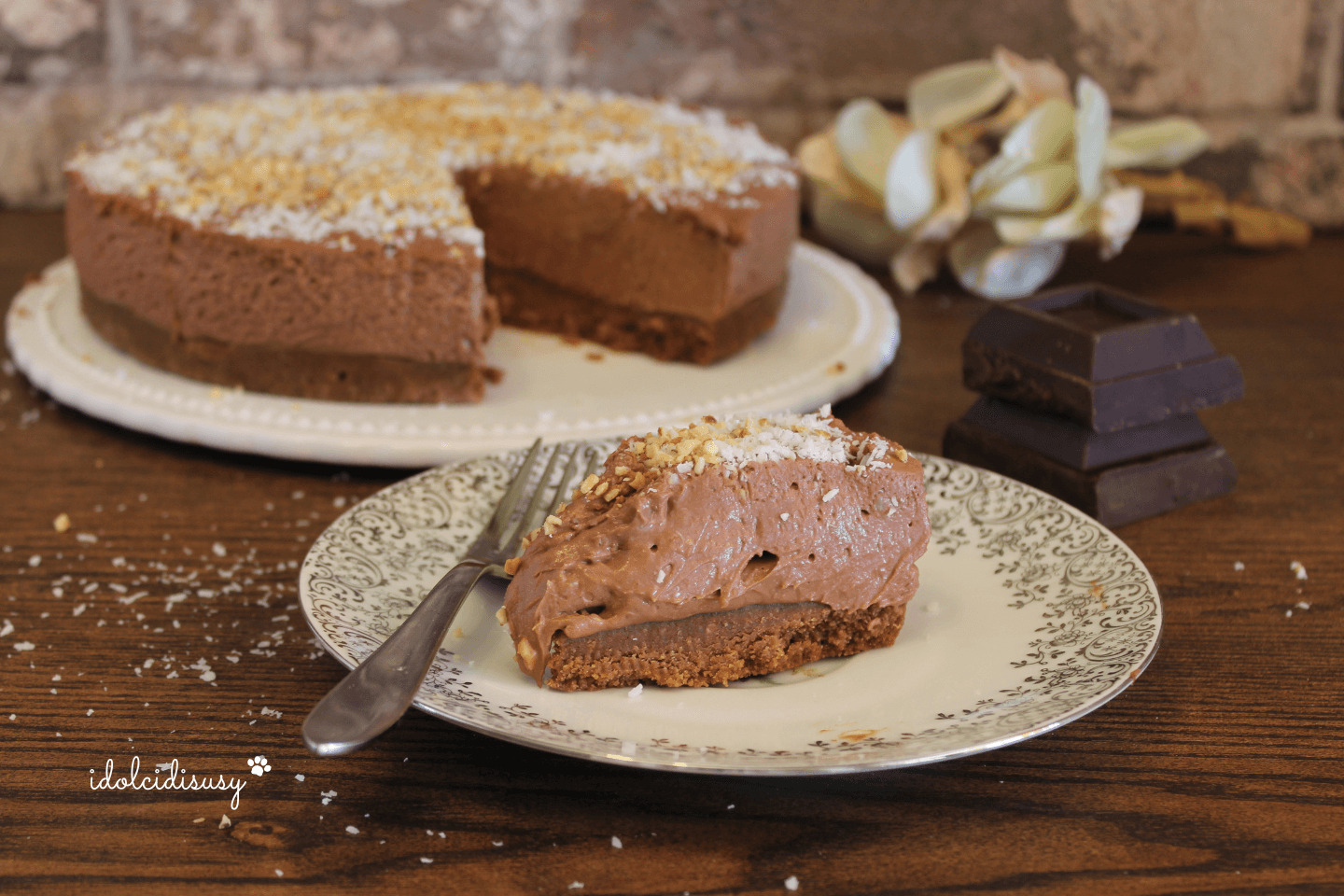 Fetta di cheesecake al cioccolato con base di biscotti e granella di nocciole su piatto decorato