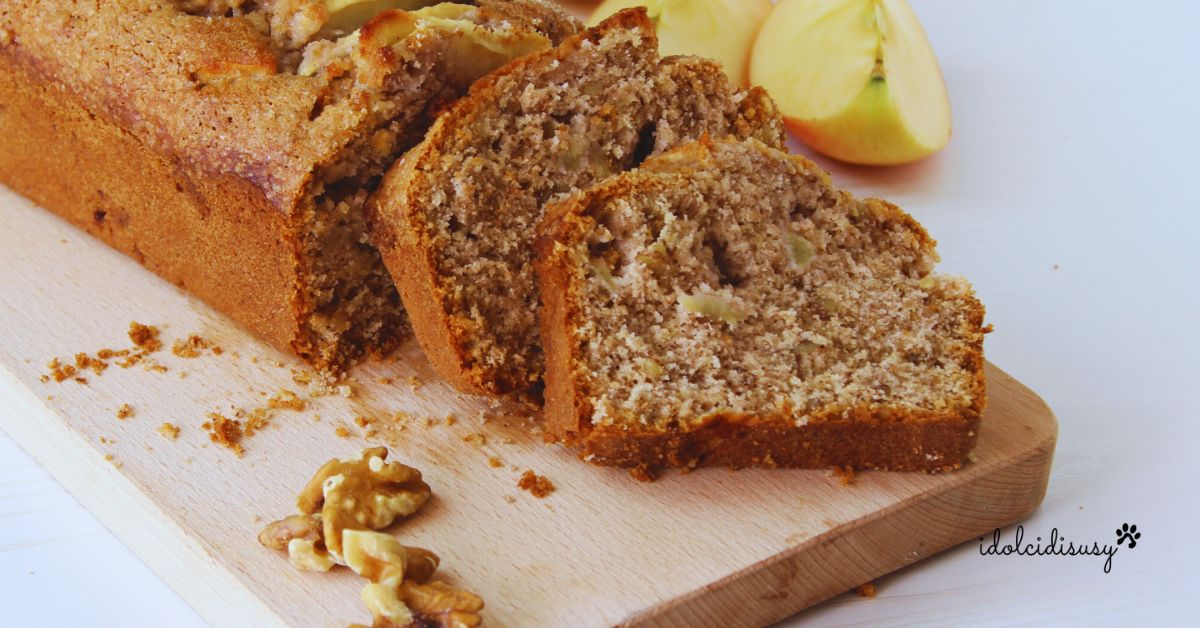 Plumcake mele e noci soffice senza burro, tagliato a fette su tagliere di legno con mele e noci sullo sfondo.