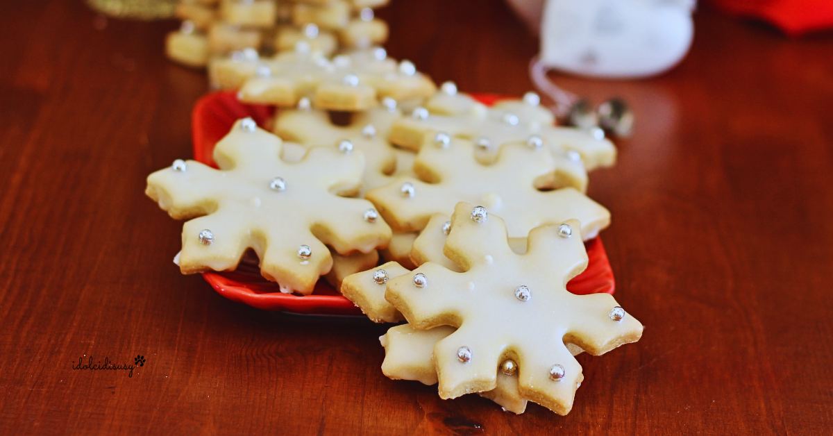 Biscotti fiocco di neve decorati con glassa bianca e palline di zucchero argentate, serviti su un vassoio rosso natalizio