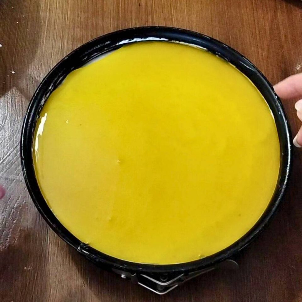 Versare la copertura al limone tiepida sulla cheesecake cremosa, creando una superficie liscia e lucida

