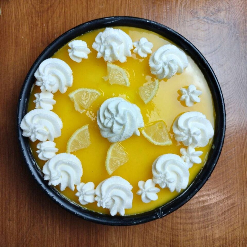 Cheesecake decorata con ciuffetti di panna montata e fettine sottili di limone, pronta per essere servita

