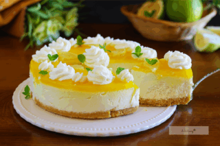 Fetta di cheesecake al limone con base biscotto, crema al mascarpone e copertura al limone senza gelatina, decorata con panna e limone fresco