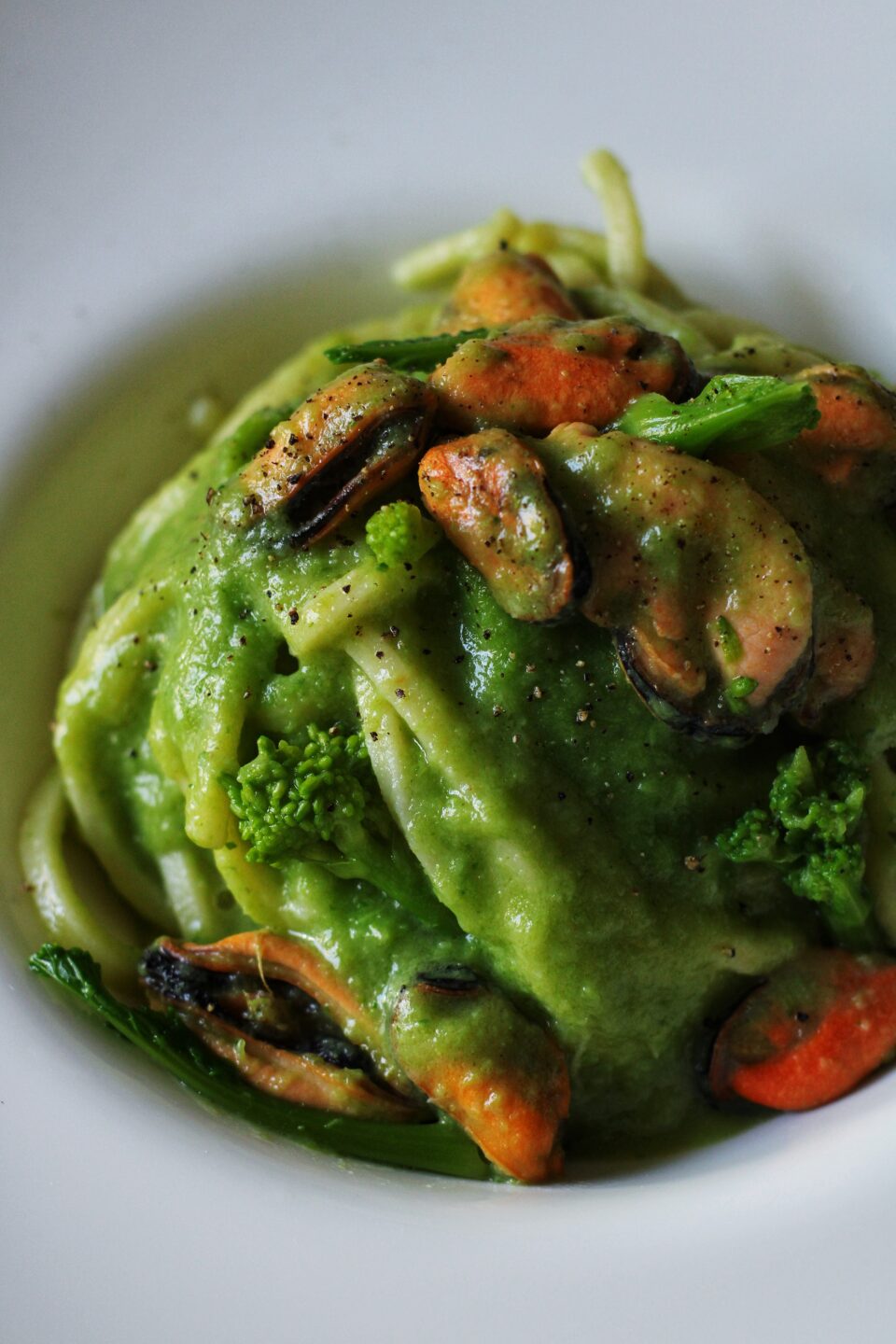 Piatto di troccoli con crema di cime di rapa e cozze, decorato con cimette verdi, olio d’oliva e pepe nero.