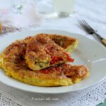 Frittata di zucchine e pomodorini tagliata a fette su un piatto bianco e tovaglia ricamata
