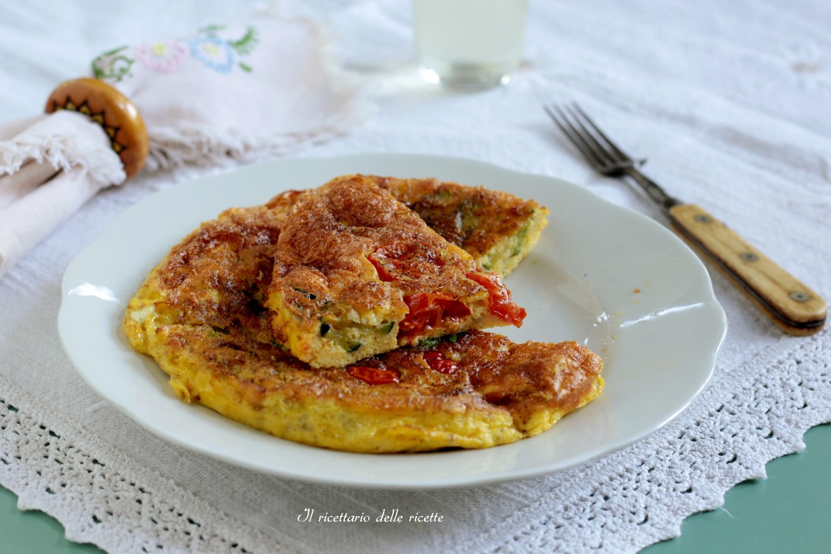 Frittata di zucchine e pomodorini tagliata a fette su un piatto bianco e tovaglia ricamata