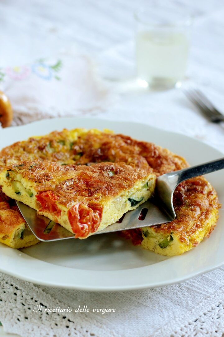 Fetta di frittata con zucchine e pomodorini sollevata con una spatola d'acciaio