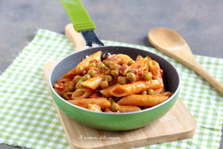 Padellina verde con penne al pomodoro e piselli su tagliere di legno