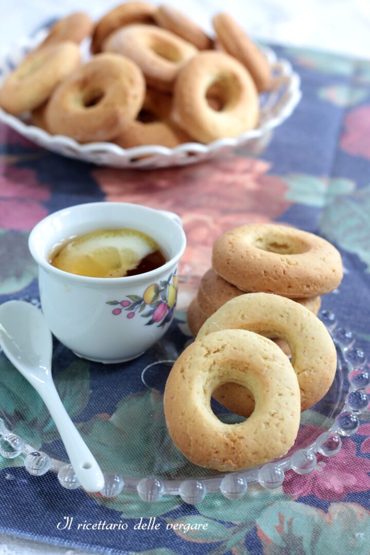 Ciambelline morbide alla panna senza burro impilate su un piattino di vetro vicino a una tazzina di tè.