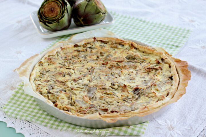 Torta salata con carciofi e ricotta in crosta di pasta sfoglia servita su un canovaccio a quadretti.