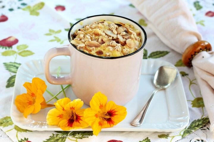 Mug cake al limone e mandorle in tazza rosa su vassoio bianco con fiori arancioni