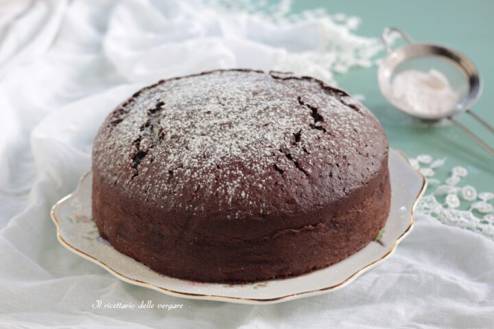 Torta nuvola al cacao intera su un piatto con colino per zucchero a velo sullo sfondo