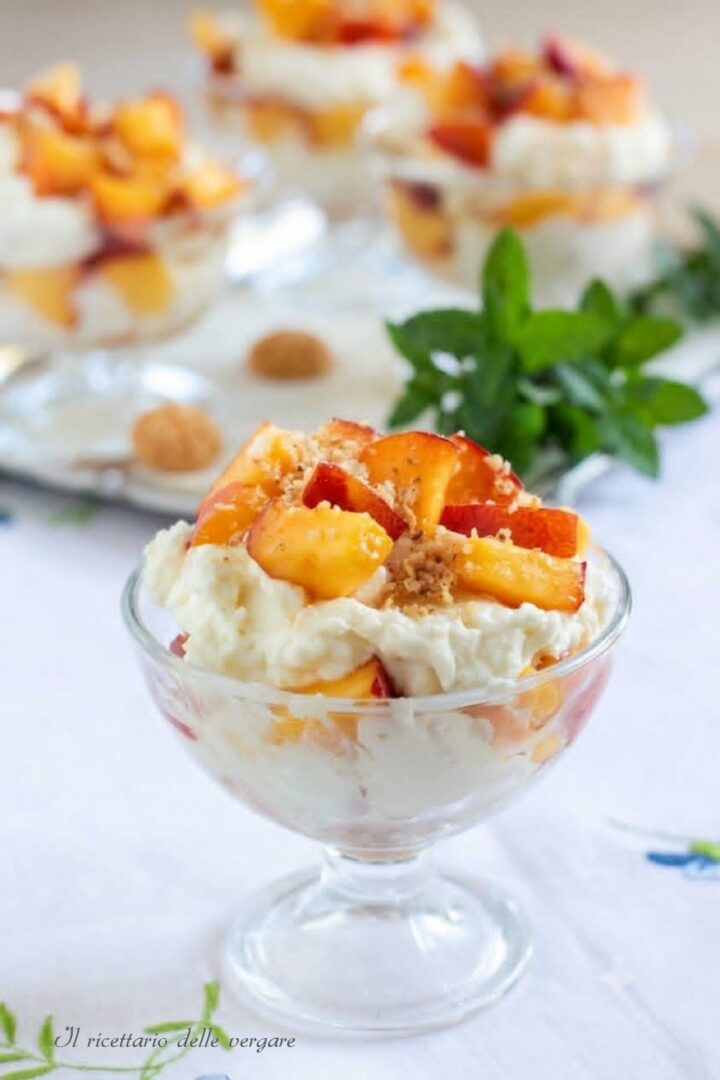 Inquadratura verticale delle coppette pesche ricotta e mascarpone con amaretti sbriciolati e foglioline di menta