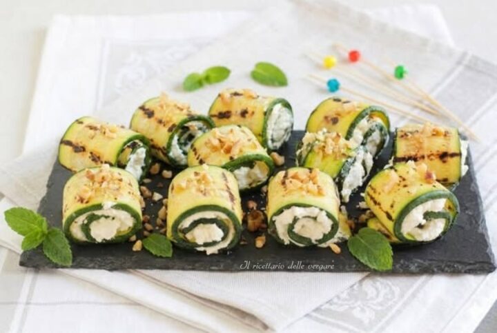 Rotolini di zucchine grigliate ripieni di crema di robiola su vassoio di ardesia con granella di noci e menta fresca.