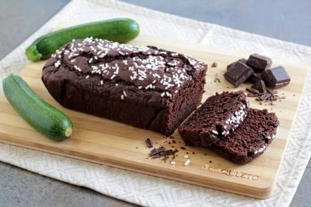 Plumcake Zucchiciok al cioccolato e zucchine intero e a fette su un tagliere di legno con zucchine fresche.