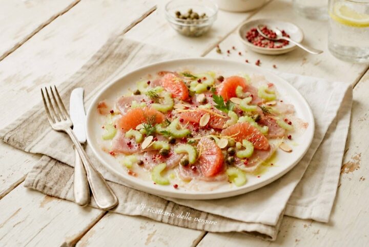 Carpaccio di tonno fresco con spicchi di pompelmo rosa, sedano e capperi su un piatto bianco