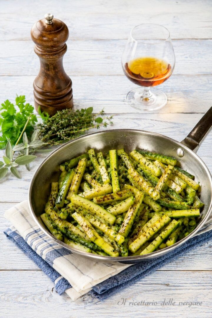 Inquadratura verticale di cetrioli a bastoncino in padella con bicchiere di cognac e macinapepe