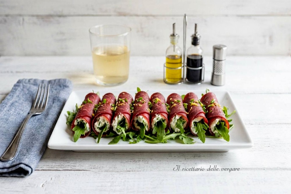 Vassoio bianco con involtini di bresaola rucola e caprino su un tavolo di legno chiaro