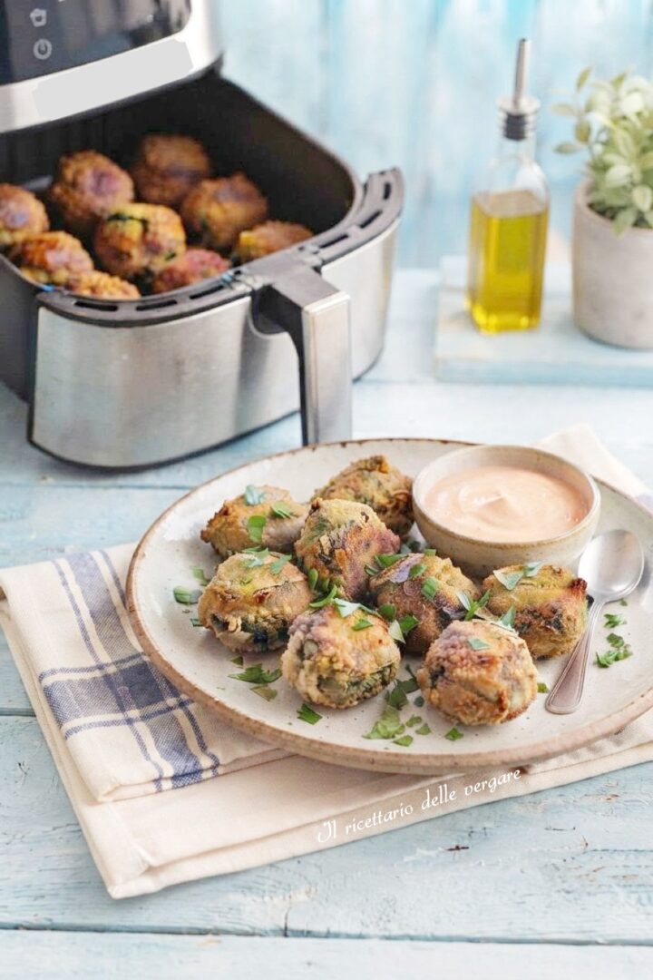 Polpette di carne dorate e croccanti cotte nella friggitrice ad aria disposte su un piatto da portata.