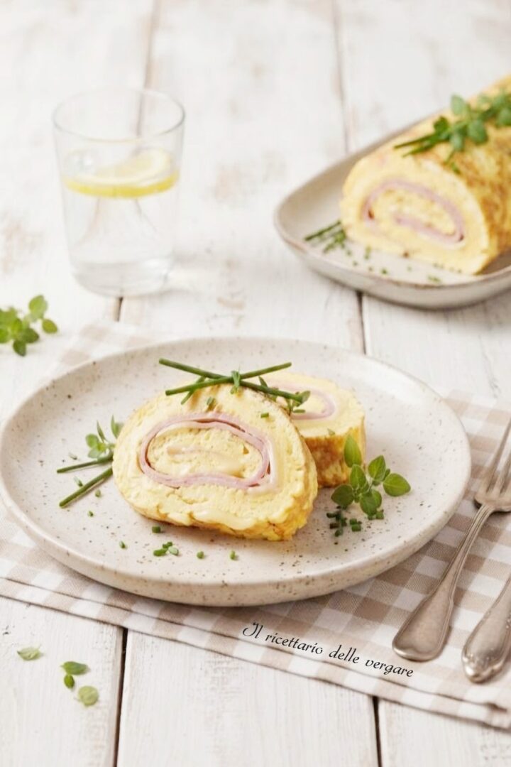 Inquadratura verticale di due fette di rotolo di frittata al forno con prosciutto e formaggio guarnite con erba cipollina