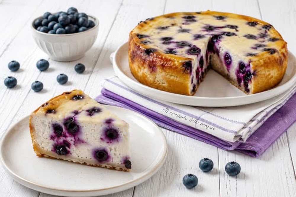 Torta soffice con robiola e mirtilli intera e a fette su un tavolo bianco