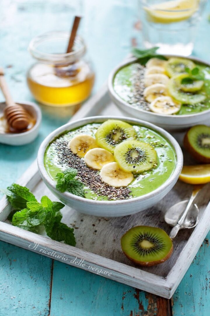 Due ciotole di frullato verde al kiwi e banana decorate con semi di chia e menta fresca