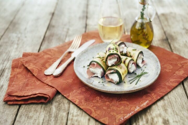 Un piatto rustico con involtini di zucchine grigliate ripieni di philadelphia e prosciutto cotto, serviti su un tavolo in legno.