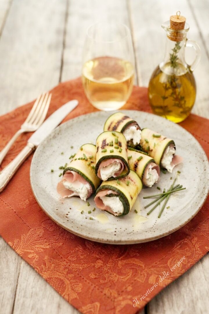 Inquadratura verticale dall'alto di involtini di zucchine grigliate farciti con formaggio cremoso spalmabile e prosciutto.