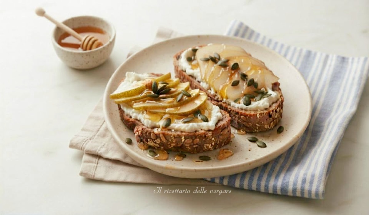 Fette di pane integrale tostato con formaggio caprino spalmato, fettine di pere, semi di zucca e un filo di miele.