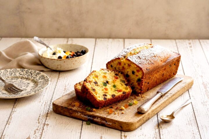 Fetta di plumcake alla ricotta con canditi e gocce di cioccolato su un tagliere in legno.