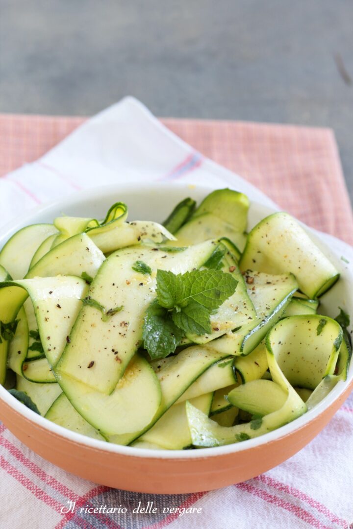 Nastri di zucchine marinate a crudo con olio e limone guarniti con foglioline di menta, serviti in una ciotola di terracotta.