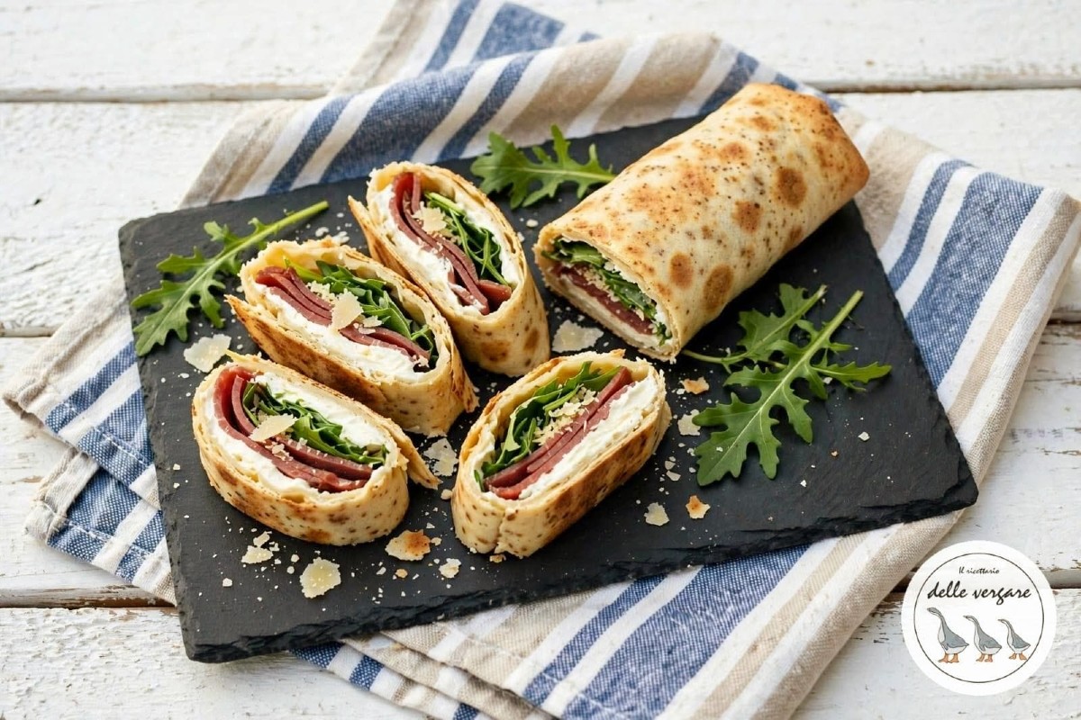 Rotolo di piadina freddo tagliato a girelle con bresaola, rucola e scaglie di parmigiano su un tagliere di lavagna nera