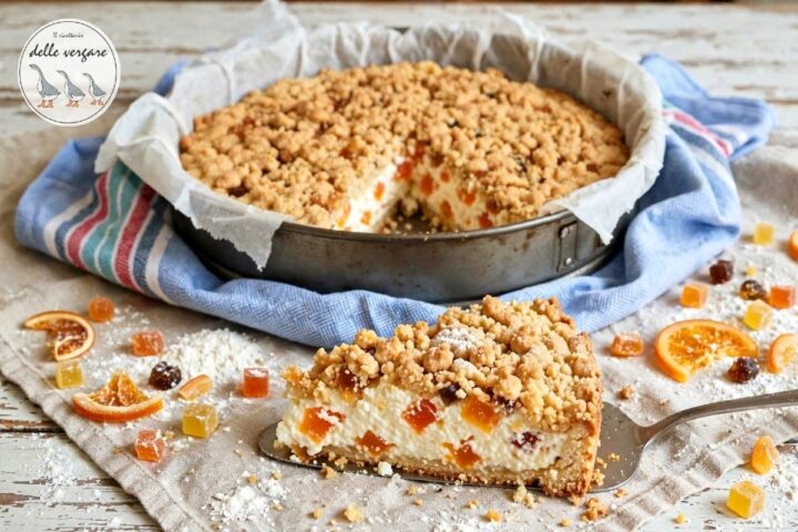 Fetta di sbriciolata con ricotta e canditi servita su una paletta da dolce, con la torta intera sullo sfondo