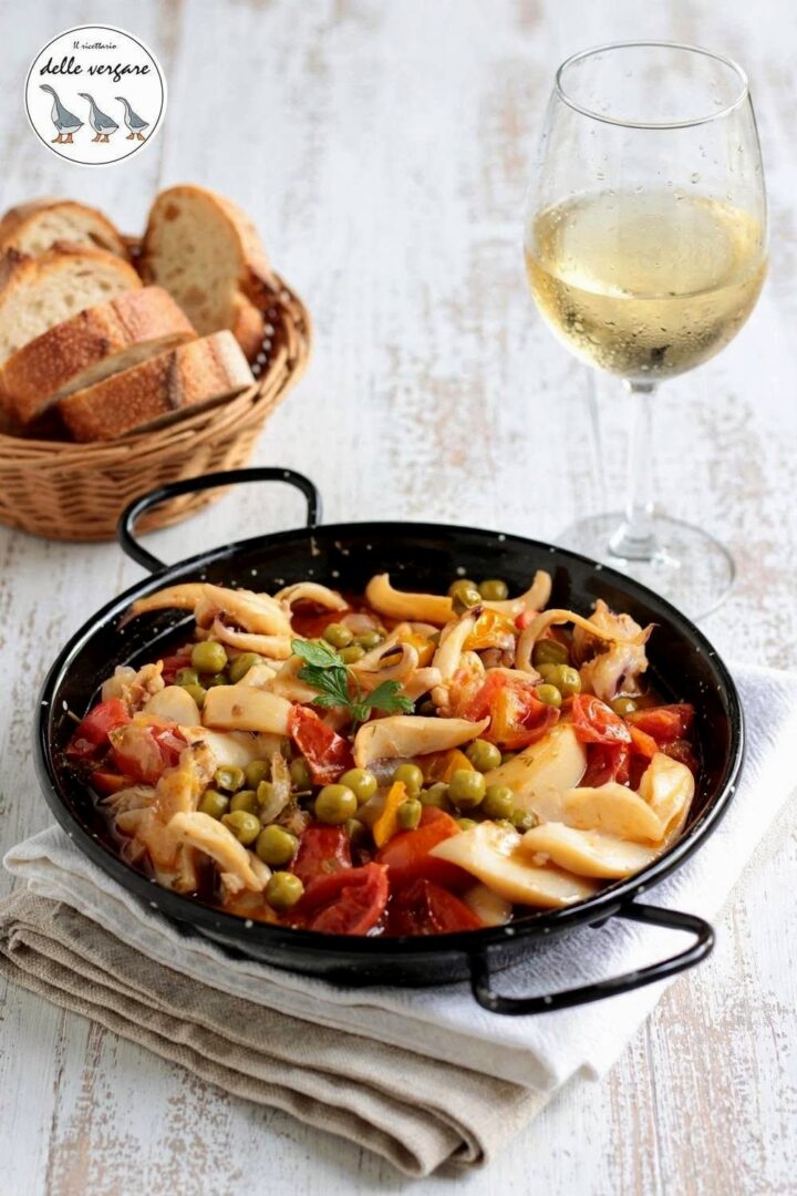 Tegamino di seppie in umido con piselli accompagnato da fette di pane e un bicchiere di vino bianco.