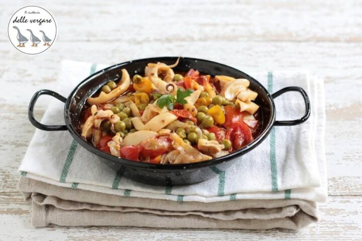 Seppie in umido con piselli, pomodorini freschi e peperoncino servite in un tegamino nero.