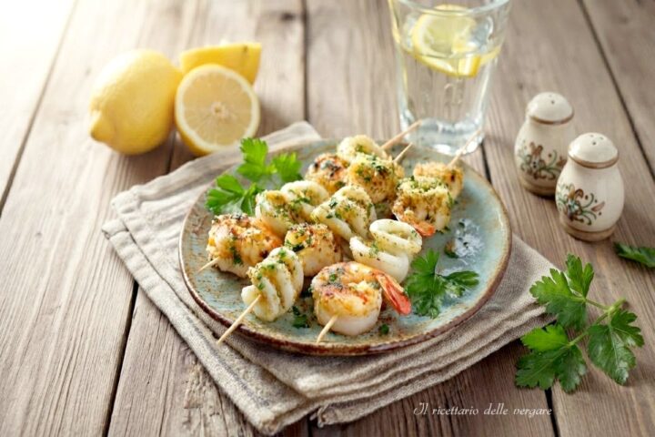 Spiedini di gamberi e calamari grigliati al limone e prezzemolo disposti su un piatto.