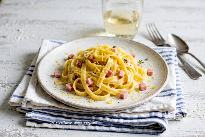 Un piatto di tagliatelle cremose al limone con cubetti di prosciutto cotto, scorza di limone grattugiata e foglioline di timo.