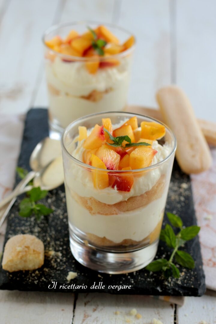 nquadratura verticale di un bicchiere di tiramisù alle pesche con pezzetti di frutta fresca in superficie