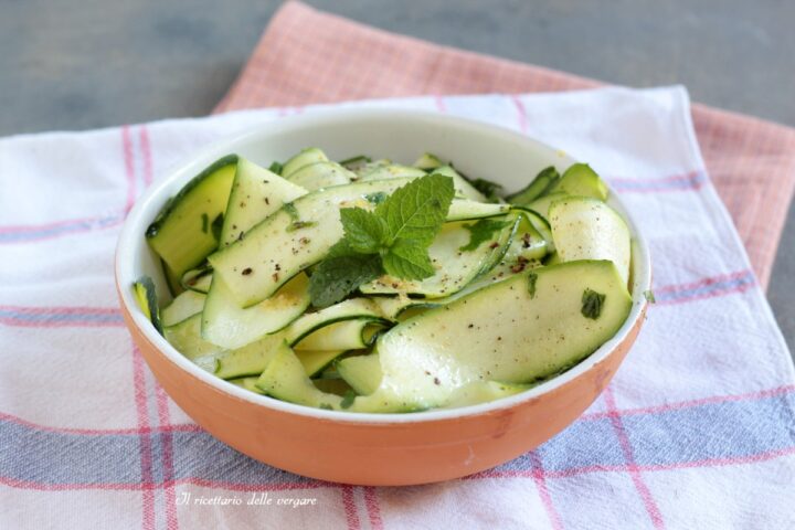Insalata di nastri di zucchine crude marinate con olio, limone e foglioline di menta fresca in una ciotola.