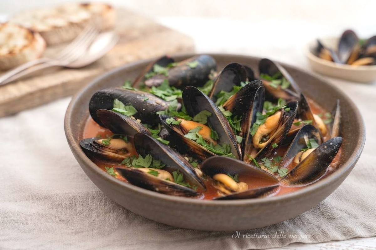 Un piatto di zuppetta di cozze piccante al pomodoro fresco guarnito con prezzemolo tritato e servito con pane tostato.