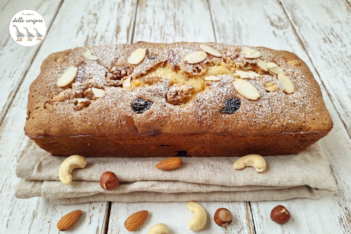 Un plumcake dorato e soffice con soli tuorli d'uovo, uvetta e mandorle a lamelle visto in orizzontale su un tavolo di legno bianco.