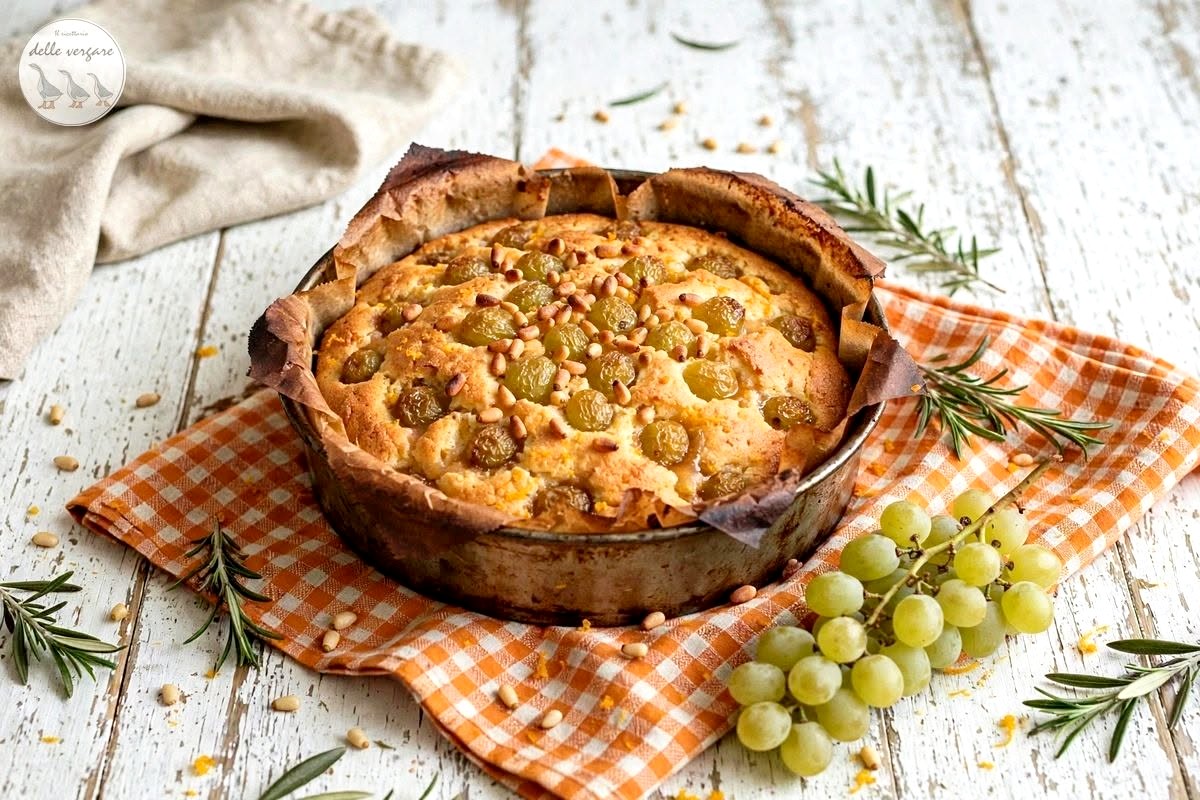 Torta soffice all'uva bianca e pinoli in una tortiera rustica con acini freschi e rosmarino sul tavolo