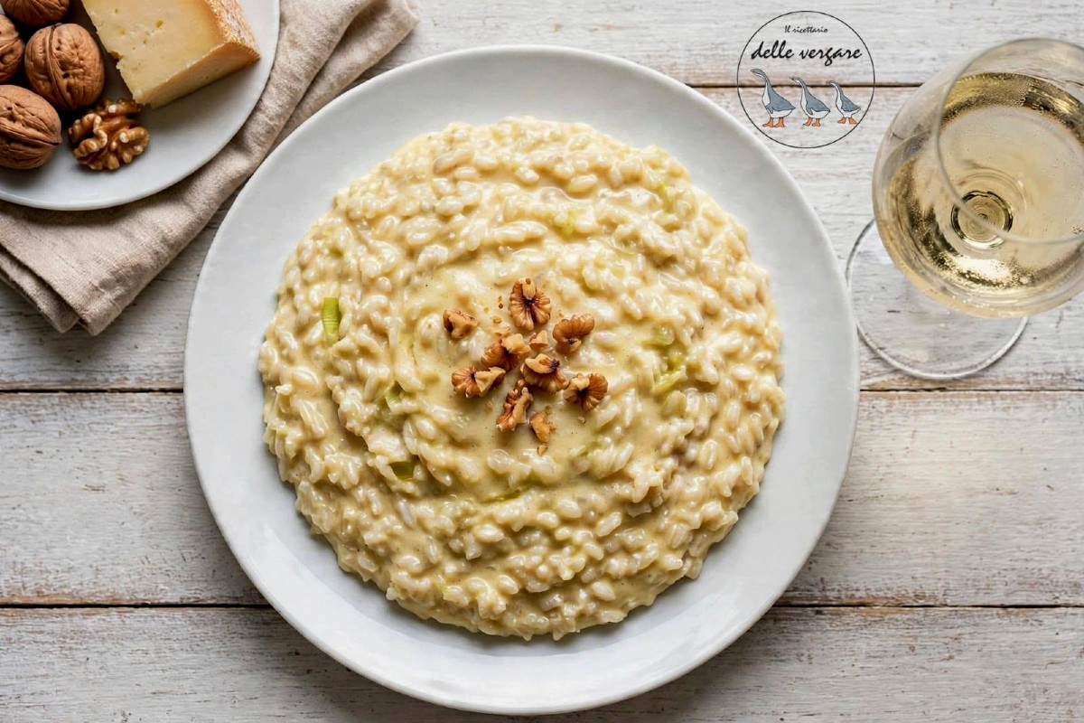 Risotto cremoso con porri e taleggio impiattato all'onda e decorato con gherigli di noci tostate in superficie.