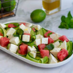 Primo piano dell'insalata di anguria con formaggio tipo feta, cetriolo e foglie di basilico.