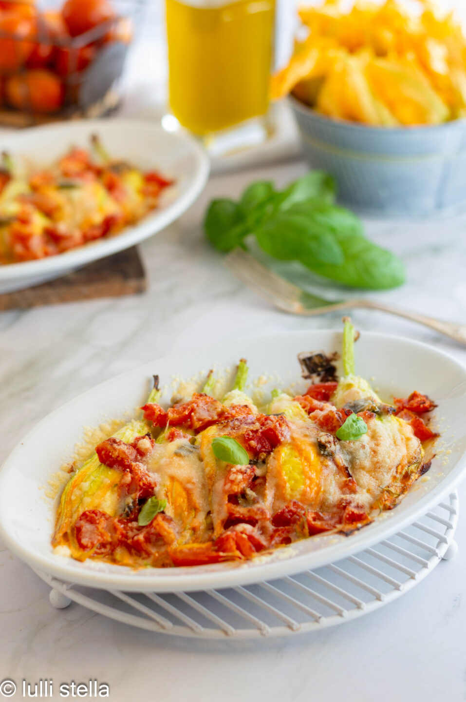 Fiori di zucca ripieni di ricotta gratinati al forno serviti con pomodorini saltati e basilico fresco.