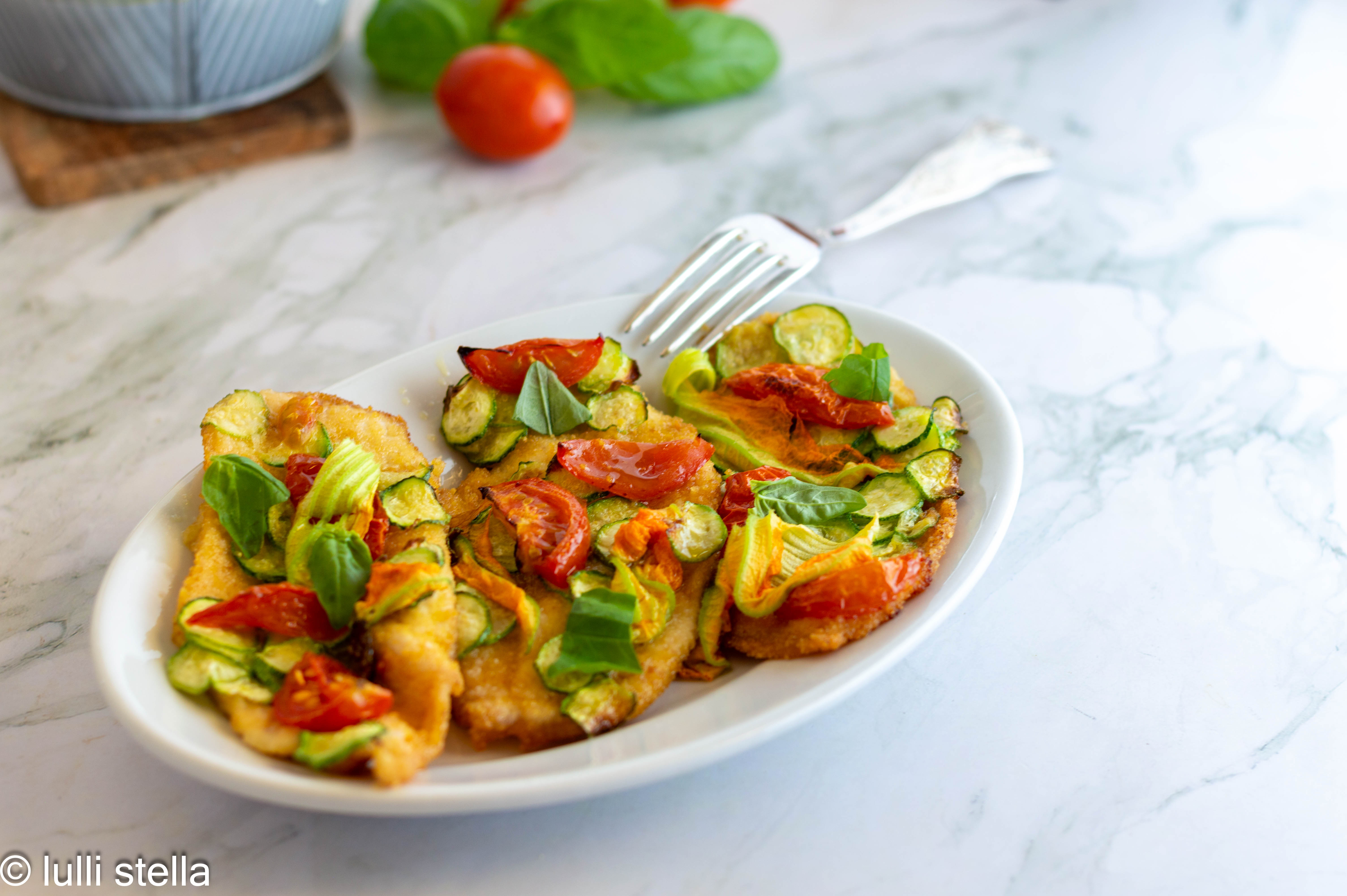 Petto di pollo panato al forno con zucchine e pomodorini servito su piatto ovale