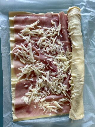 pasta sfoglia farcita con prosciutto e provolone grattugiato pronta per essere arrotolata