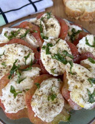 Dettaglio di una caprese estiva con pomodori maturi, mozzarella fresca e basilico preparata in 5 minuti