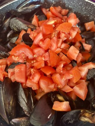 Pomodori freschi aggiunti alle cozze durante la preparazione della pasta con le cozze.