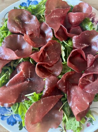 Bresaola disposta sulla rucola condita prima di aggiungere le scaglie di parmigiano.